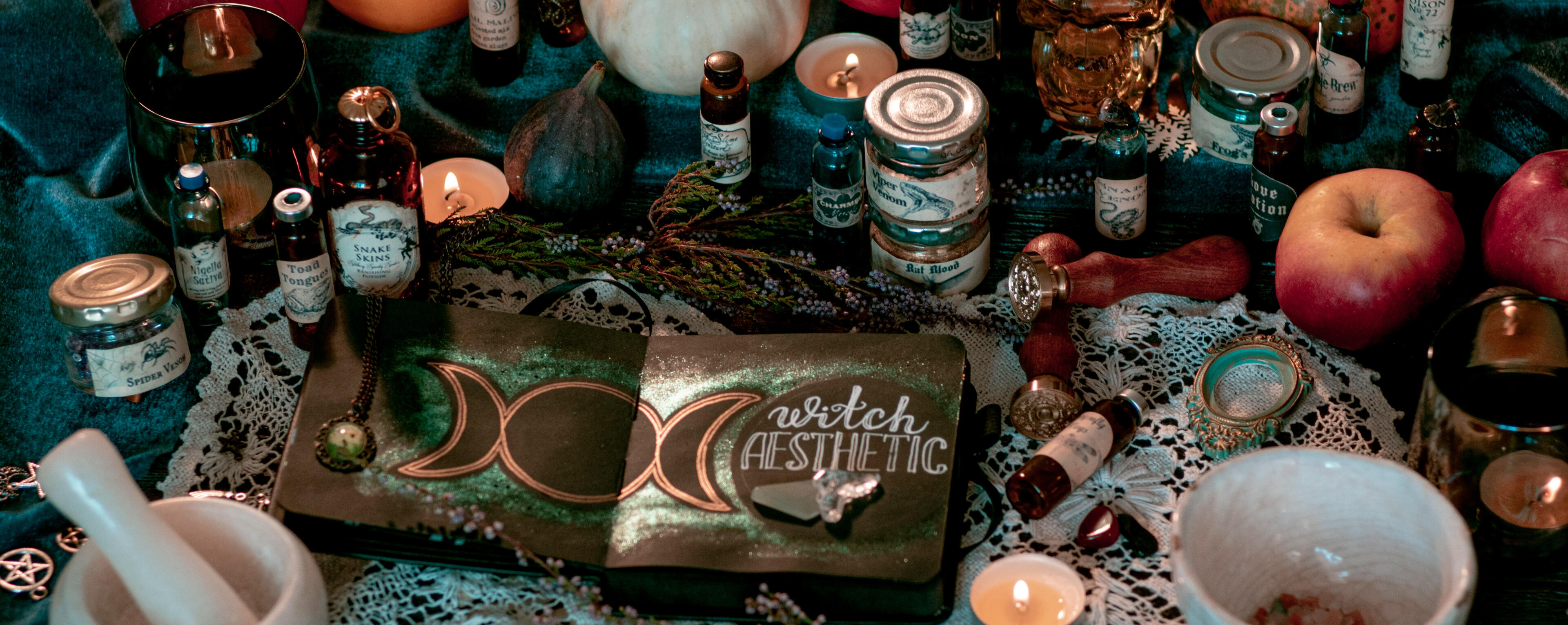 A table with a wide variety of witchy related jars. There's a notebook open that states "witchy aesthetic" on the table with the moon goddess symbol.